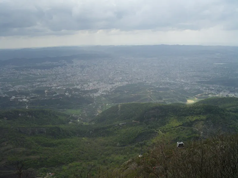 Hazy view over Tirana and the surrounding hills from Mount Dajti with a cable car in the foreground.