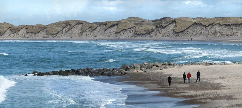 Waves rolling onto the sandy beach at Nørre Vorupør beneath tall dunes on the Danish North Sea coast.