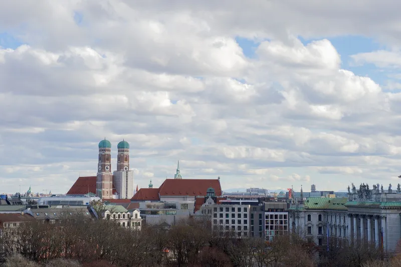 The twin towers of the Frauenkirche rising above the Munich skyline under a cloudy sky.