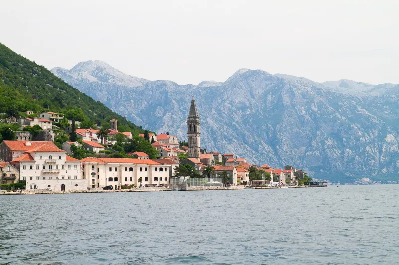The bell tower and stone houses of Perast on the Bay of Kotor beneath steep mountains.