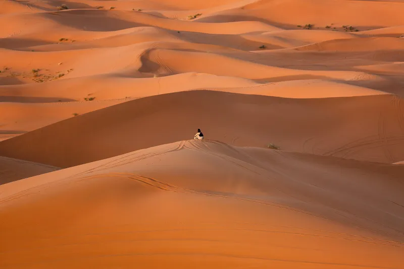 Orange sand dunes of the Sahara in Morocco at sunset with a lone figure on a ridge.